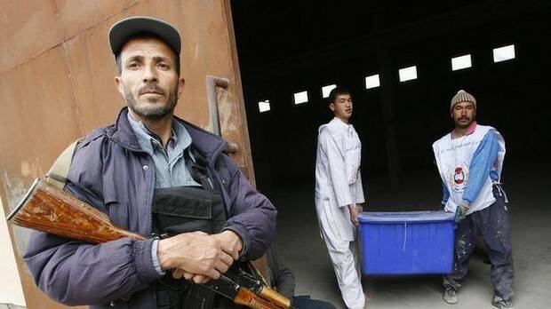 Afghan election commission workers carry a ballot box as a police officer stands guard.